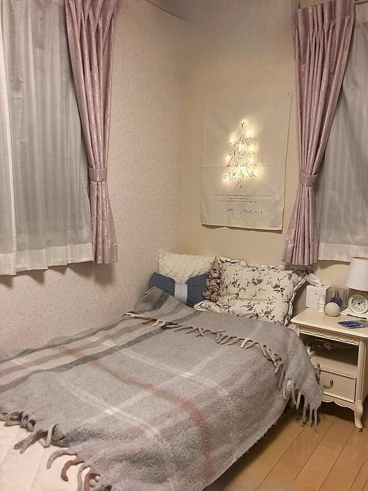 ベージュと淡いピンクの色調の小さな寝室、ベッドと枕、ナイトテーブル、クリスマスの飾りが配置された雰囲気のあるインテリア