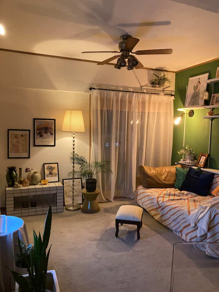 Natural color and green accented living room featuring a large sofa, stool, and warm lighting creating a cozy atmosphere