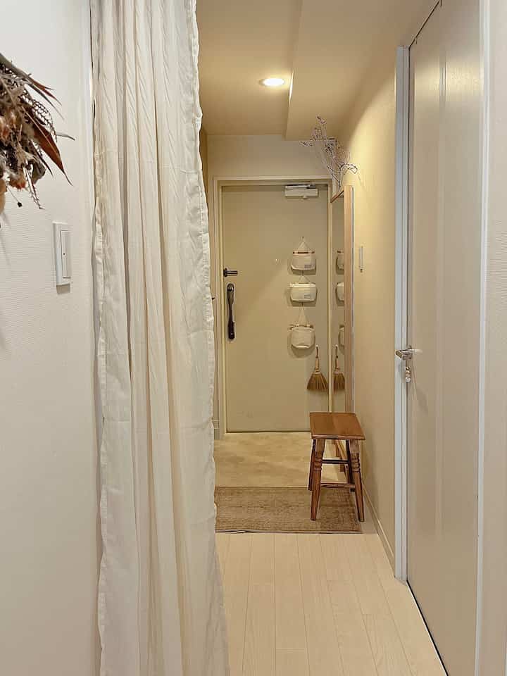 ナチュラルカラーの狭い玄関、ウッドスツールとコーナー収納が配置されたミニマルな雰囲気のインテリア