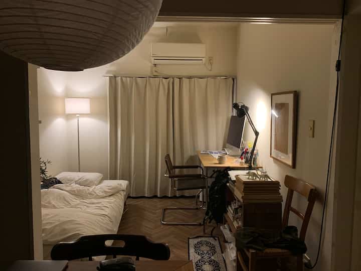 白と茶色のトーンのワンルーム寝室とホームオフィス、カーテンとフロアランプが調和した落ち着いた雰囲気のインテリア