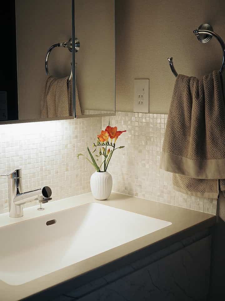 Warm beige and white small powder room featuring shell tile backsplash, chrome towel rack, and decorative vase creating cozy atmosphere