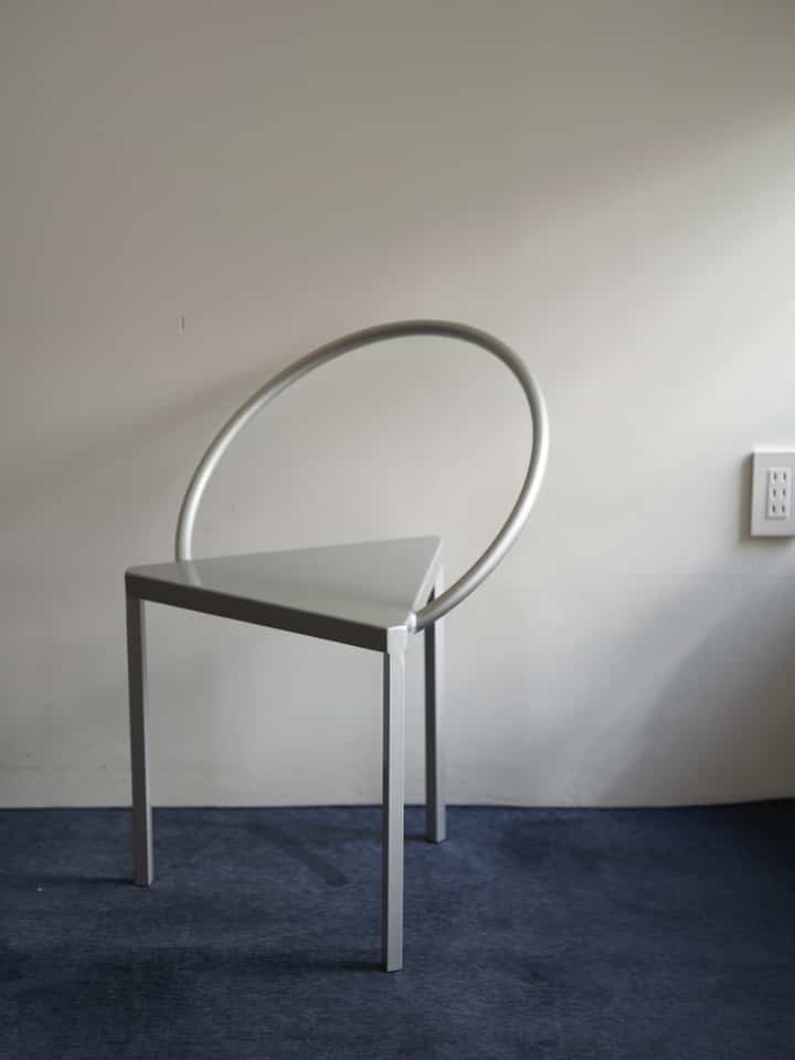 青いカーペットとインダストリアルスタイルの独特な三角形の金属製アームチェアが配置されたモダンなワンルーム空間