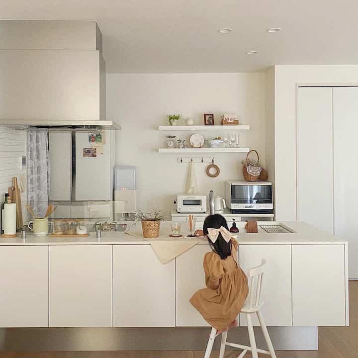 明るくナチュラルな色調のキッチンスペース、白い家具と木製アクセント、椅子に座る子供がいる印象的な空間