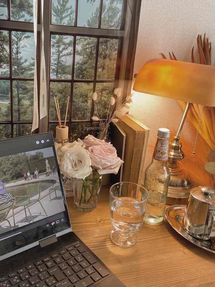 ナチュラルなブラウン色調のホームオフィス、木製のデスク上に黄色いテーブルランプと花瓶、グラスが配されて落ち着いた雰囲気のインテリア