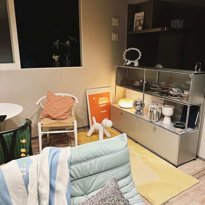 ナチュラルカラーの壁と床、オレンジのアクセント、ソファ、サイドボードが配置された温かみのあるリビングとダイニングの空間