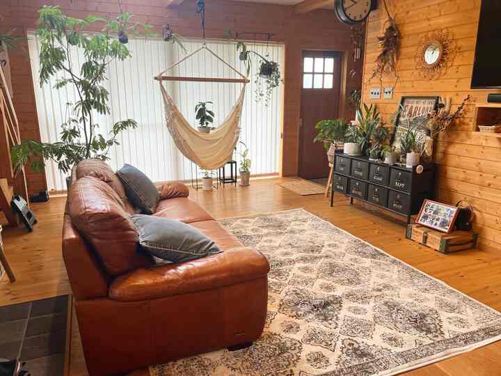 ナチュラルな木目調のリビング、大きなブラウンレザーのソファとオーガニックなハンモックチェアが配置された落ち着いた空間