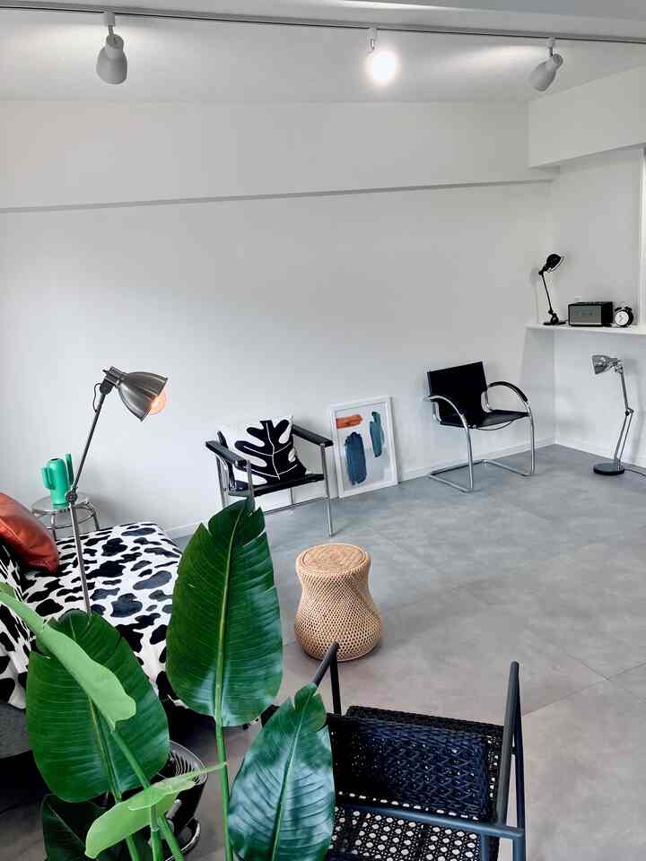 グレーの床とメタルチェア、ラタンのスツール、シンプルな照明が配置された印象的なミッドセンチュリーモダンのリビングルーム