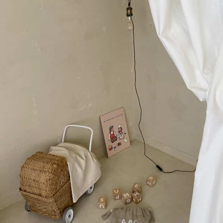 Beige natural tone walls and floor, wheeled rattan basket, alphabet blocks, and pendant light arranged in a minimalist corner space