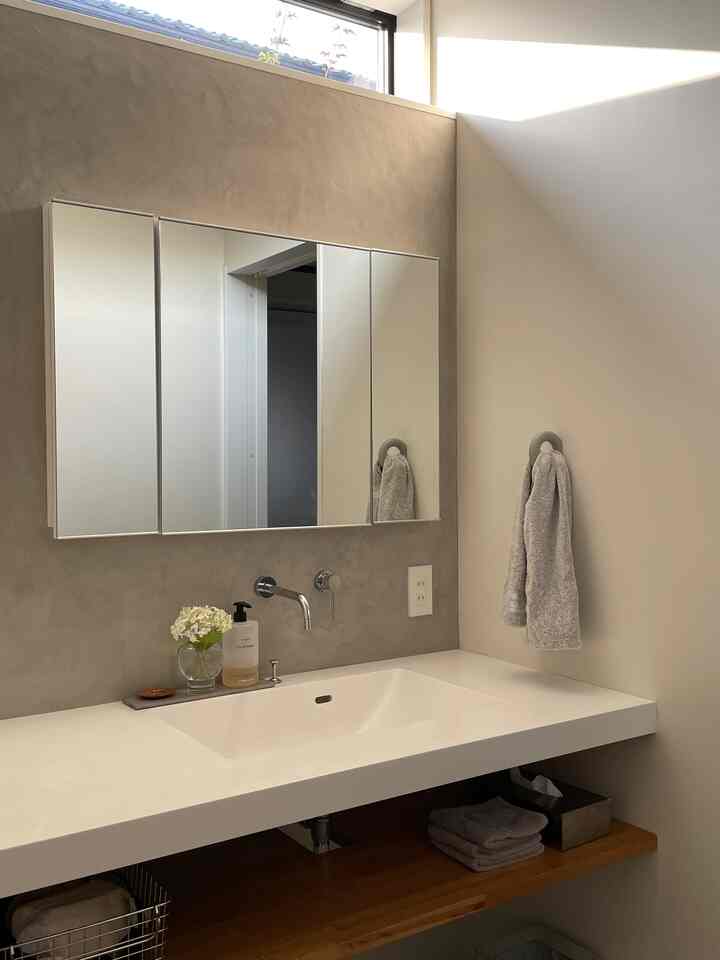 グレーのトーンの洗面所スペース、清潔感のある白い洗面台とグレーのタオル、鏡、ナチュラルモダンな印象的なインテリア