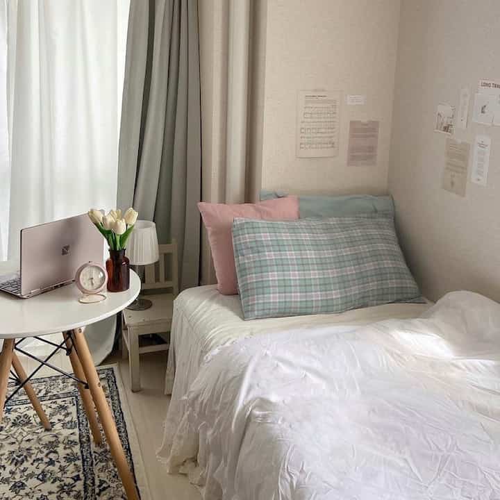 A beige and white toned bedroom featuring a bed with checkered pillows and curtains, creating a cozy and neat space