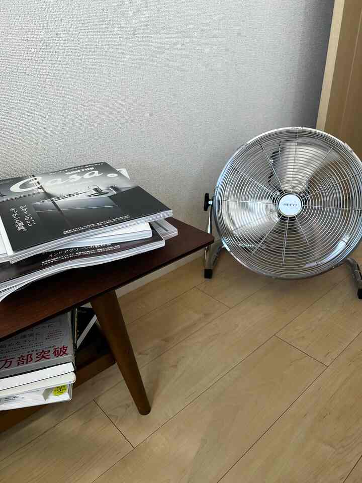 明るい木目調の床と木製デスクが配置された空間、アルミ製フロアファンがあり、シンプルで自然な雰囲気のインテリア