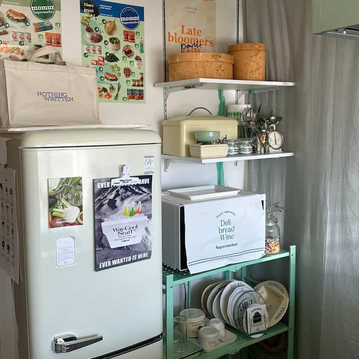 Cozy kitchen space featuring white appliances and walls, green storage shelves, and natural wood boxes with organized kitchenware