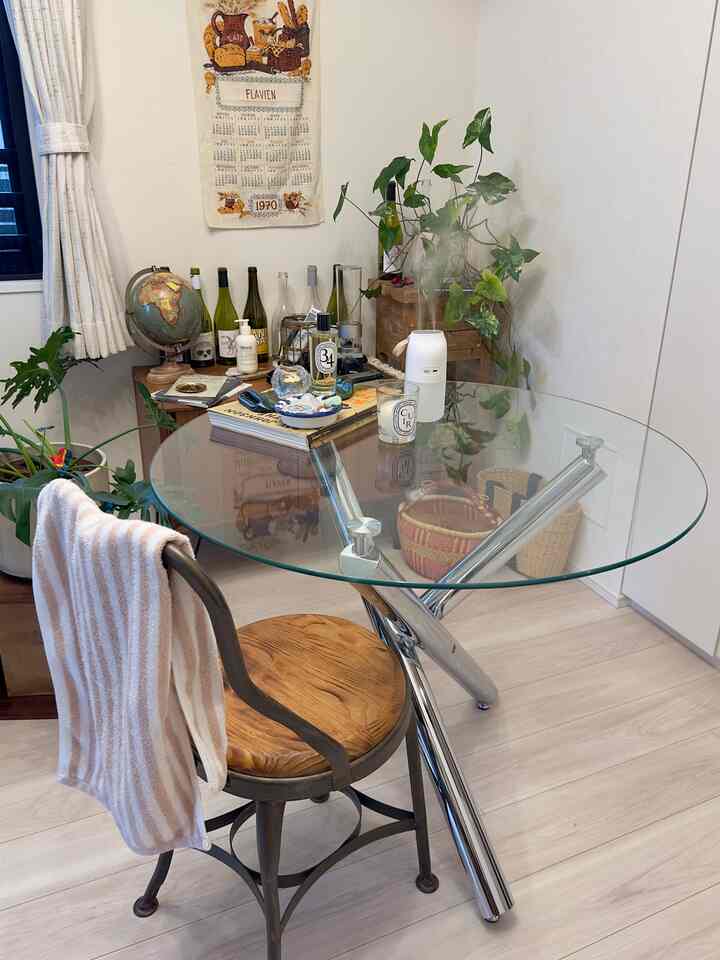 白と透明の色調のダイニング、ガラスの丸テーブルと木製の椅子、植物とキャンドルが配置された雰囲気あるインテリア