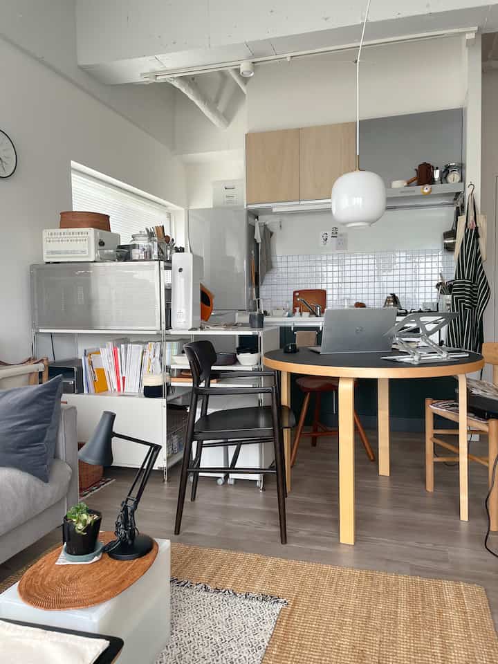 白を基調とした壁とナチュラルウッドのワンルームキッチンとリビング、丸いテーブルと様々な椅子が配置された雰囲気のあるインテリア