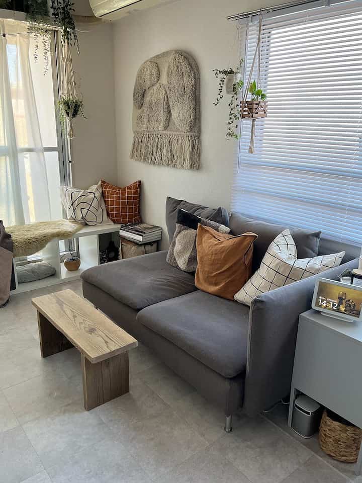 Gray sofa and wooden bench in a white-toned living room, featuring macrame wall decor and plants in a natural modern style space