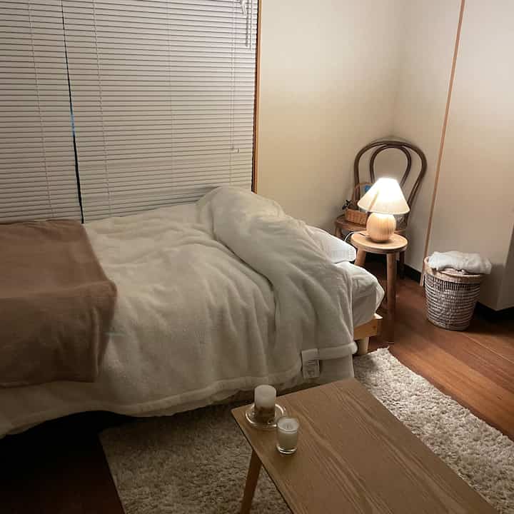 ナチュラルな色調の寝室、木製のベッドとサイドテーブル、白い寝具と暖かい照明が配置された雰囲気のあるインテリア