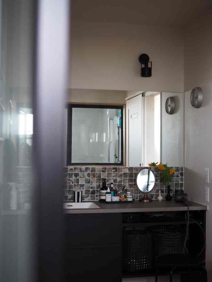 グレーとブラックのトーンが際立つバスルーム、モザイクタイルと大きな鏡、ブラケットライトが配置された印象的な空間