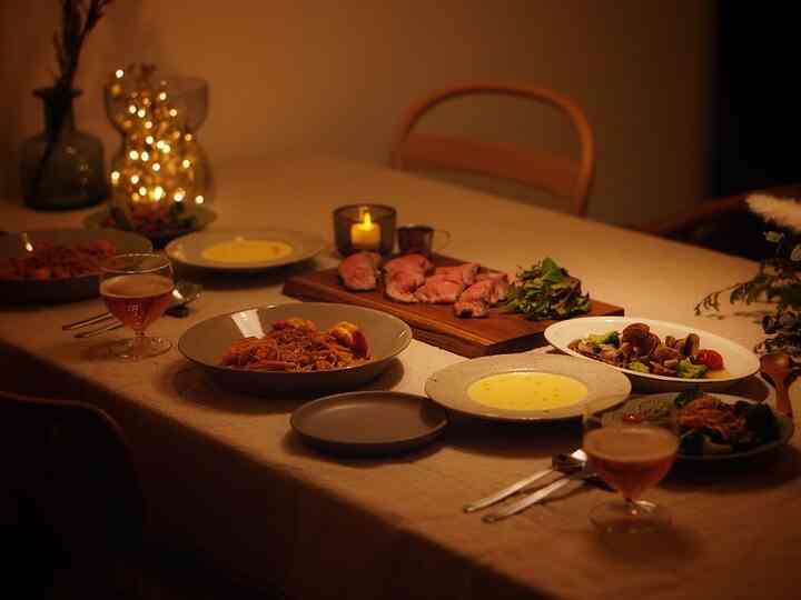 ベージュの色調のダイニング、シンプルな食器とキャンドル、花瓶が置かれた雰囲気のあるホームパーティー空間