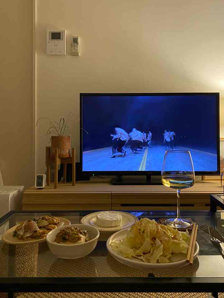 ベージュの壁とブラウンのコンソールがあるリビング、ガラスのワイングラスとプレートが置かれたコーヒーテーブル、ホームシネマのテレビが配置された温かみのある空間