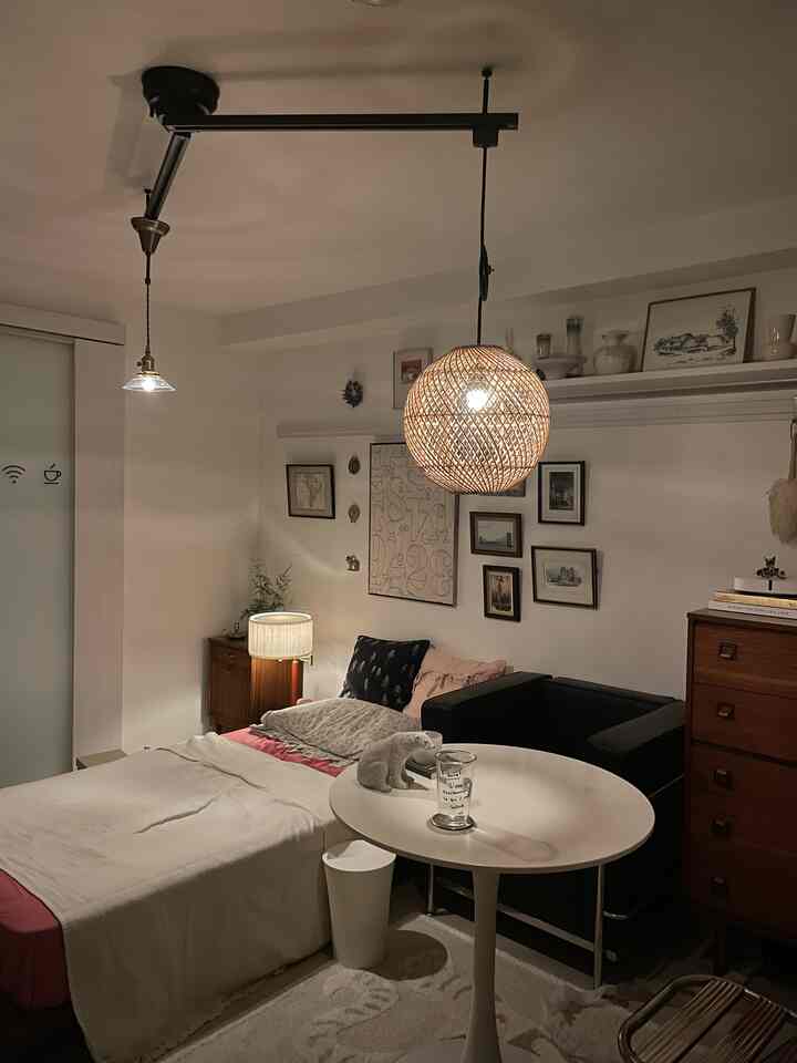 白い壁と天井に黒いソファとラタンのペンダントライトが配置された、暖かみのある一人暮らしワンルームのリビング