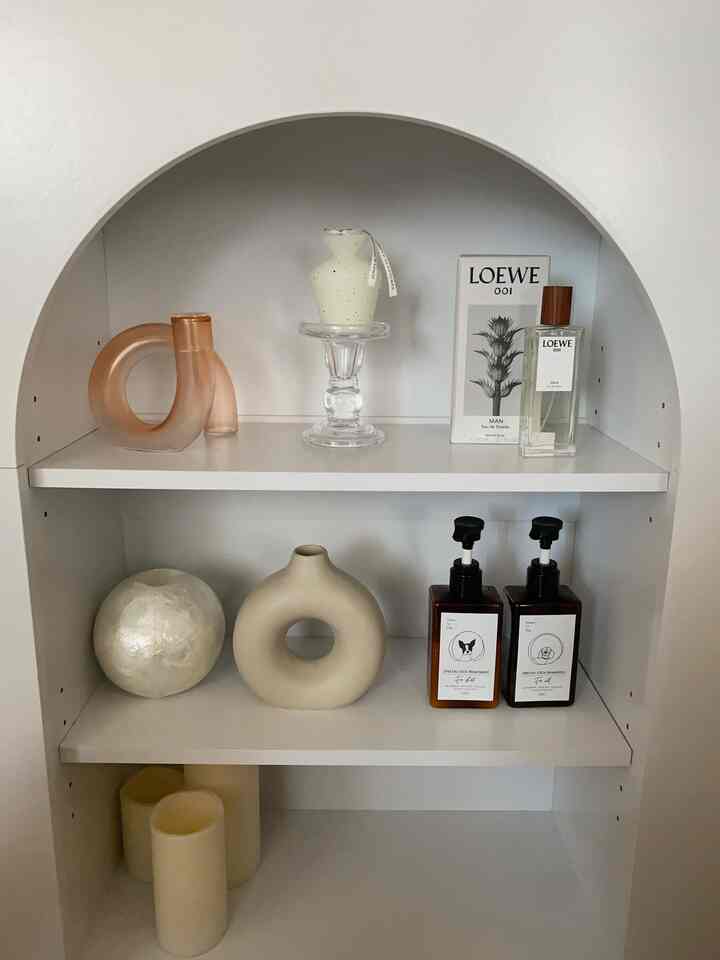 White-toned living space featuring a white shelving unit with minimal decorative items like candles and vases, creating a clean look
