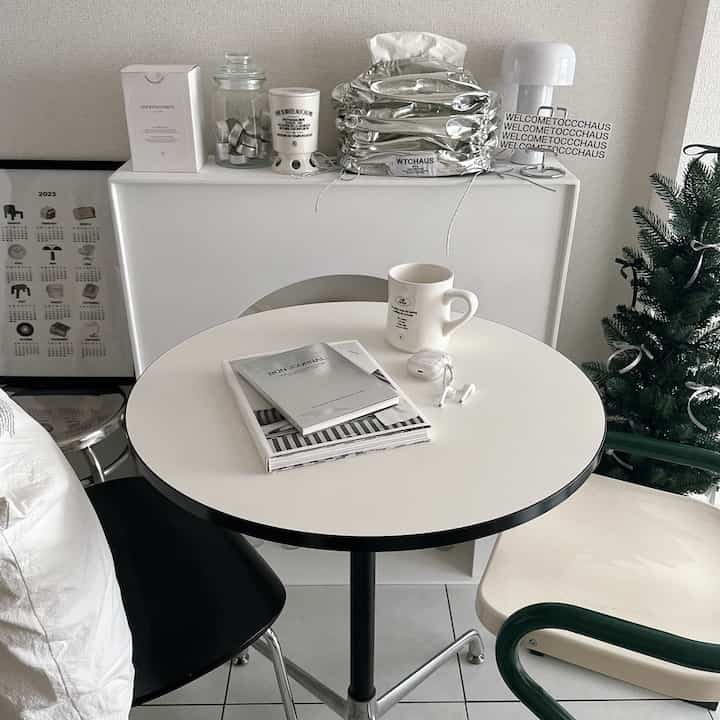 Mid-century modern styled small living space in white and silver tones, featuring a round table, curved chairs, and reading journals