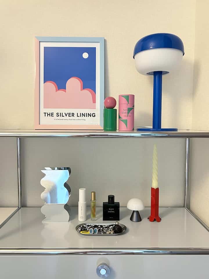 Pink and blue toned shelving featuring candles, diffusers, and a table lamp arranged neatly in a clean minimal space