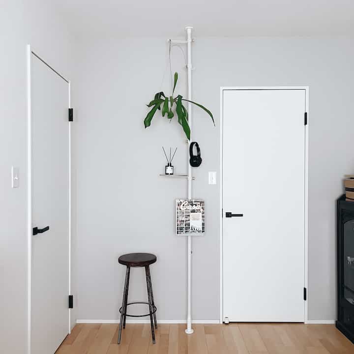 ホワイトとグレーのトーンの狭い部屋、木目調の床、スツール、植物と棚が配置されたシンプルなインテリア