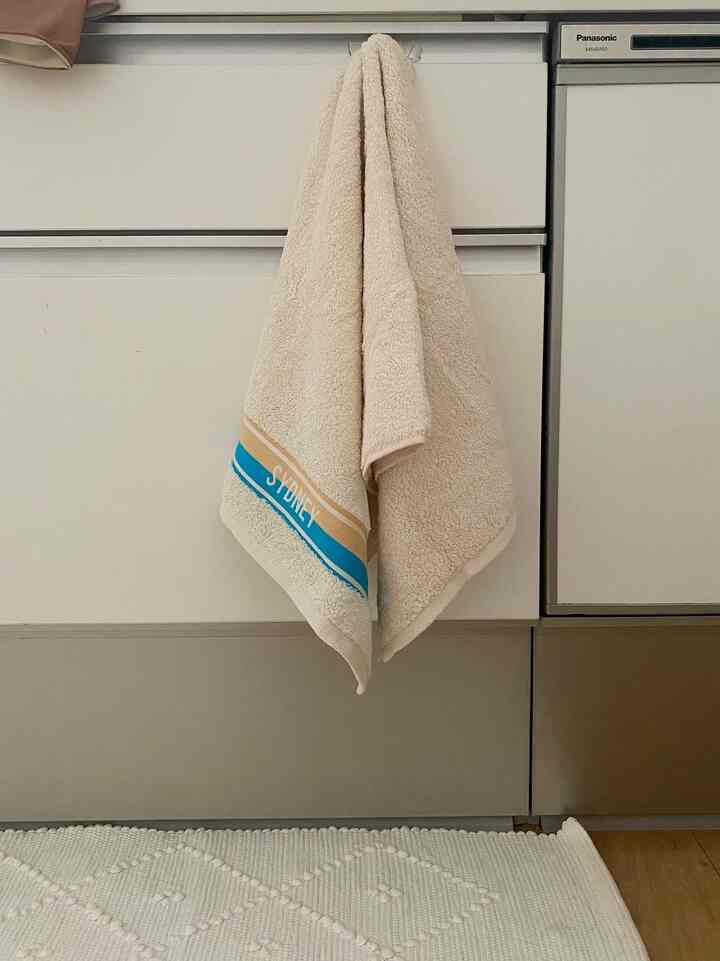 白とベージュの落ち着いた色調のバスルーム、キャビネットに掛けられたタオルとバスマットが配置された自然な雰囲気のインテリア