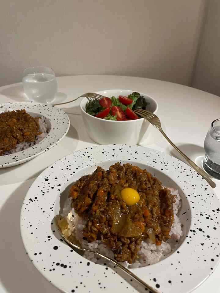 White-toned dining table featuring plates of dry curry and salad set in a clean kitchen atmosphere