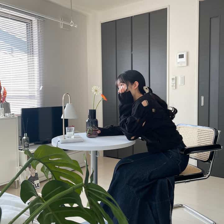 白とグレーのトーンが特徴のワンルーム、丸いテーブルに花瓶と籐製の椅子が配されたモダンで落ち着いた雰囲気のインテリア