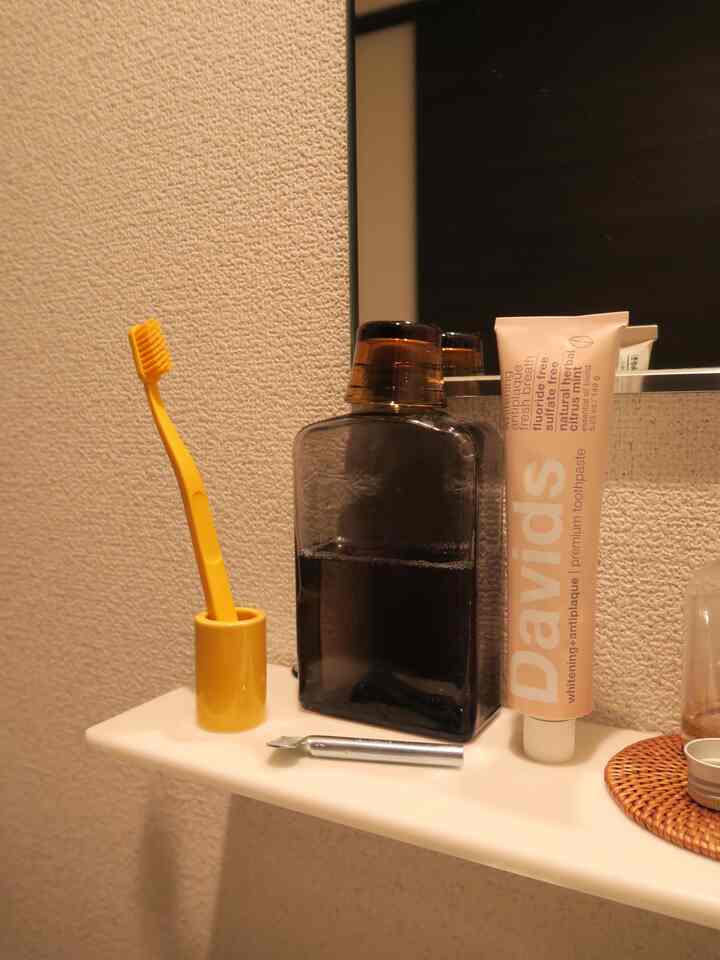 白い壁とコンパクトな棚にイエローの歯ブラシとチャコール色の瓶が置かれた小さなバスルームのインテリア