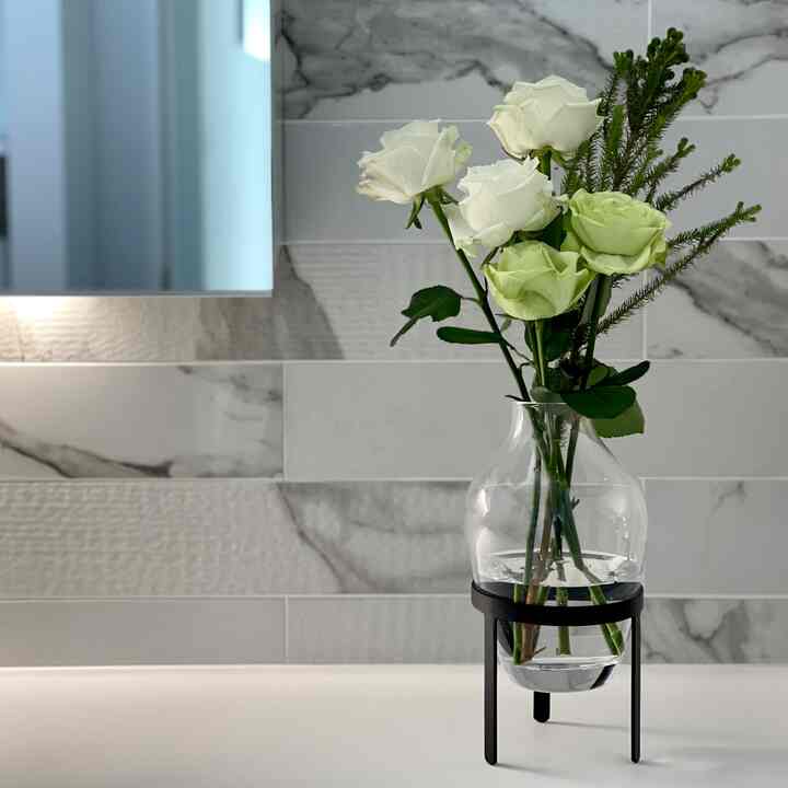 White and black toned bathroom vanity space featuring a clear glass vase with white and light green roses, showcasing a clean hotel-like interior