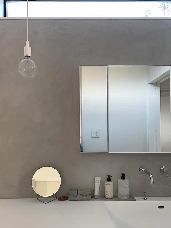 グレーのモダンなバスルーム空間、白い洗面台と壁付け蛇口、シンプルで洗練されたパウダールームのインテリア