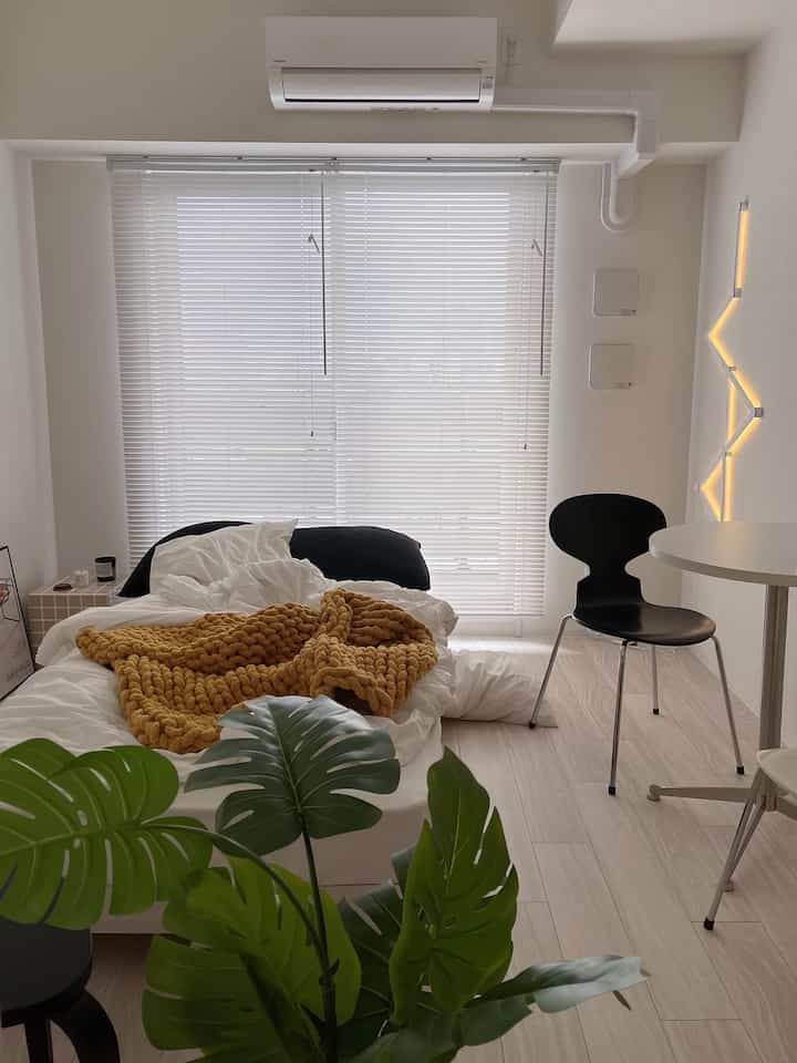 白と黄色のトーンのモダンな寝室、モンステラの植物とシンプルな家具が配置された印象的な空間