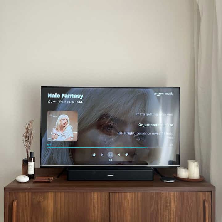 ナチュラルな木目調と白い壁が調和するワンルームのリビング、テレビ台にキャンドルとディフューザーが配された落ち着いた空間