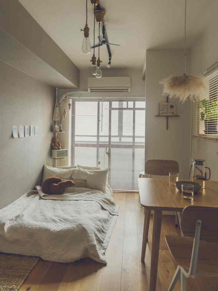 ベージュとホワイトのトーンのワンルーム、木製ダイニングテーブルとベッドが配置された自然でカフェ風の雰囲気のあるインテリア