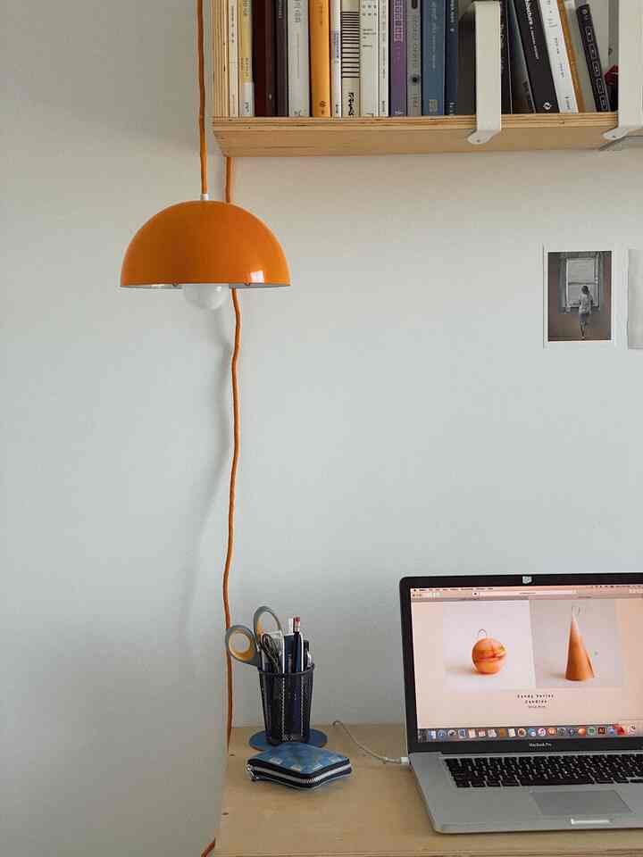 Minimal home office desk space with white walls and an orange pendant light