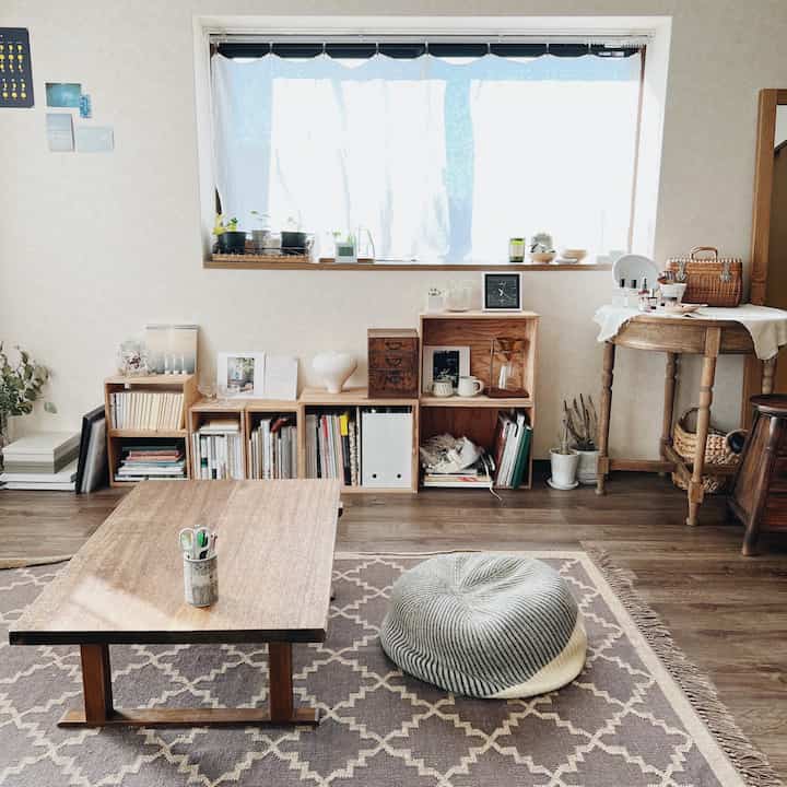 木目調のナチュラルな色合いが調和するコンパクトなリビング、中央に折りたたみローテーブルとプーフクッションが配置された清潔で居心地の良い空間