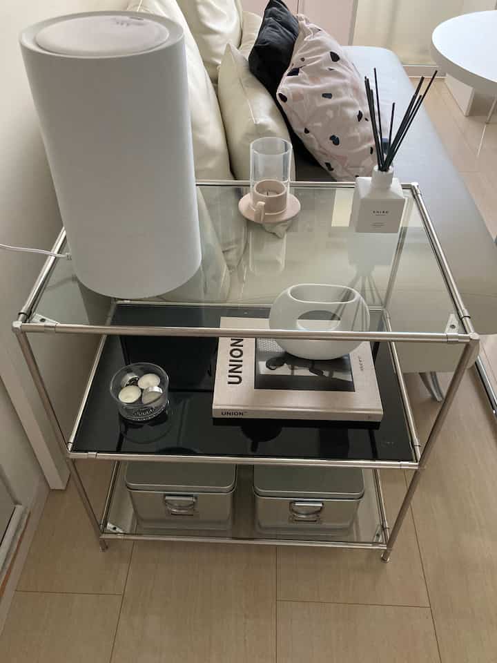 White and black toned compact living room featuring a white sofa and metal glass rack with humidifier and diffuser on top, creating a clean atmosphere