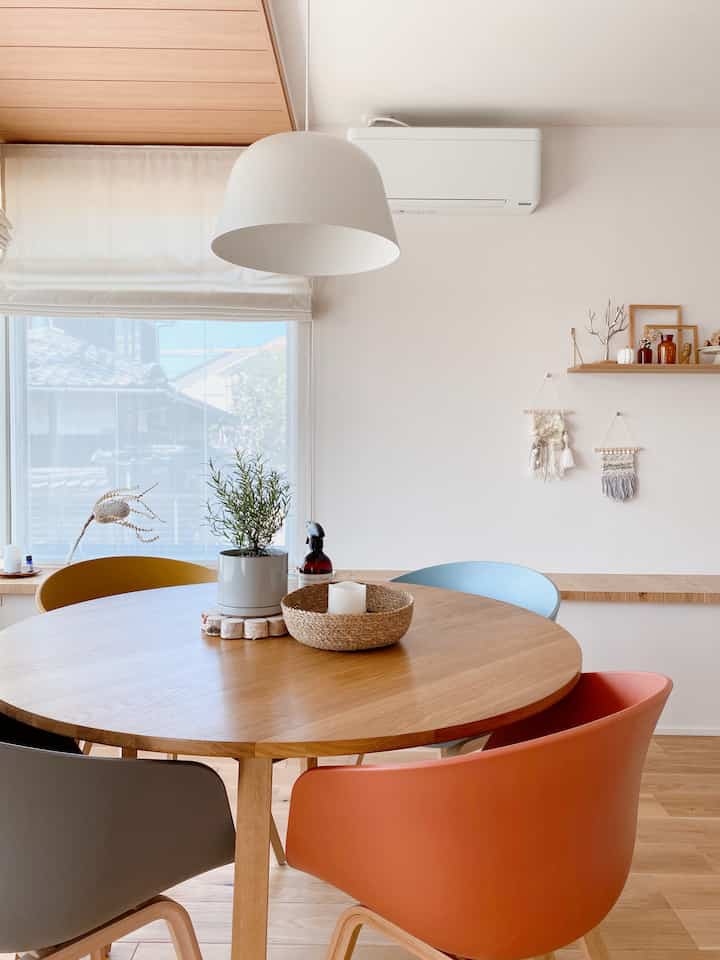 木目調と白を基調としたダイニングルーム、丸いテーブルとカラフルな椅子が配置されたミニマルな空間