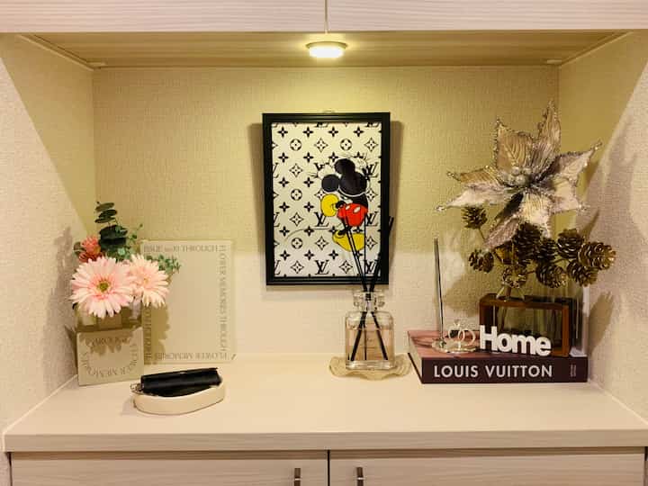 Natural tone beige entrance featuring Mickey Mouse wall art centered above a decorated surface with diffuser and floral arrangements
