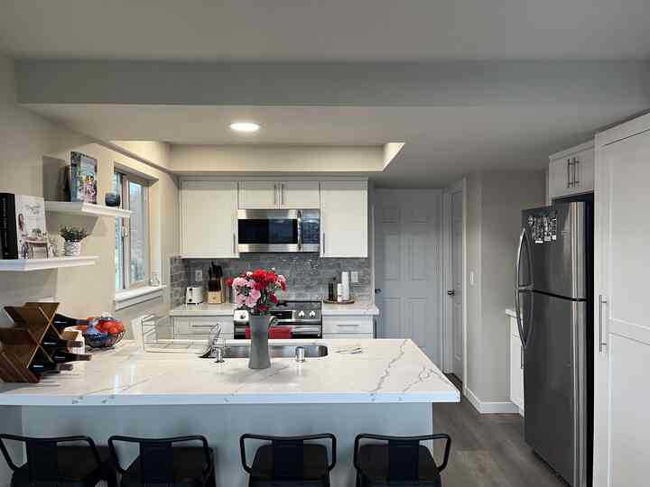Bright white-toned kitchen featuring a large island with vase centerpiece and black stools, showcasing a modern design