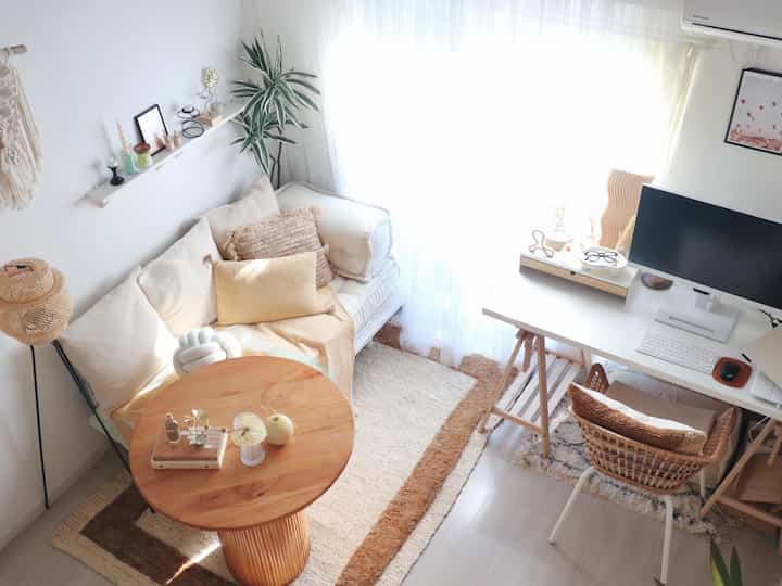 明るい白と木目調の調和した一人暮らし用ホームオフィス兼リビング、自然光と植物が暖かい雰囲気を作り出す空間