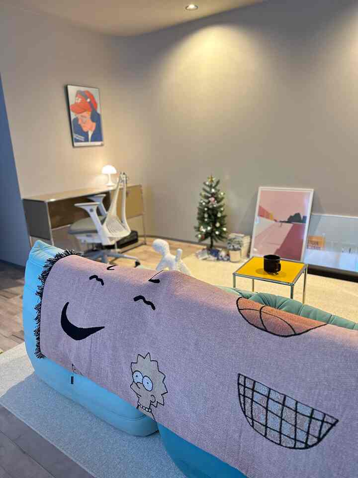 ベージュ色調の壁と床、ブルーのソファにピンクのスローが置かれた、ミニマルな雰囲気のリビング兼ワークスペース