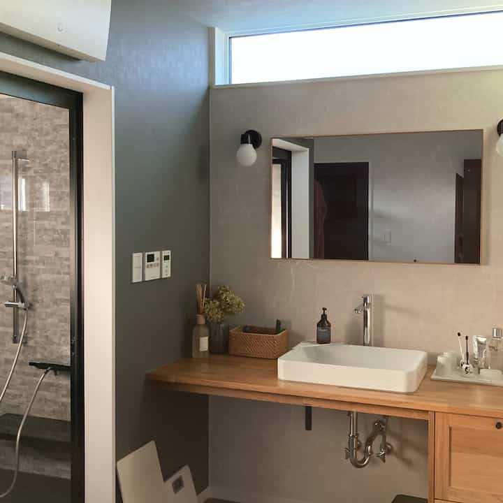 ナチュラルな木目調と白が調和したバスルーム、清潔感ある洗面台とラタンのバスケットが配置された雰囲気のある空間