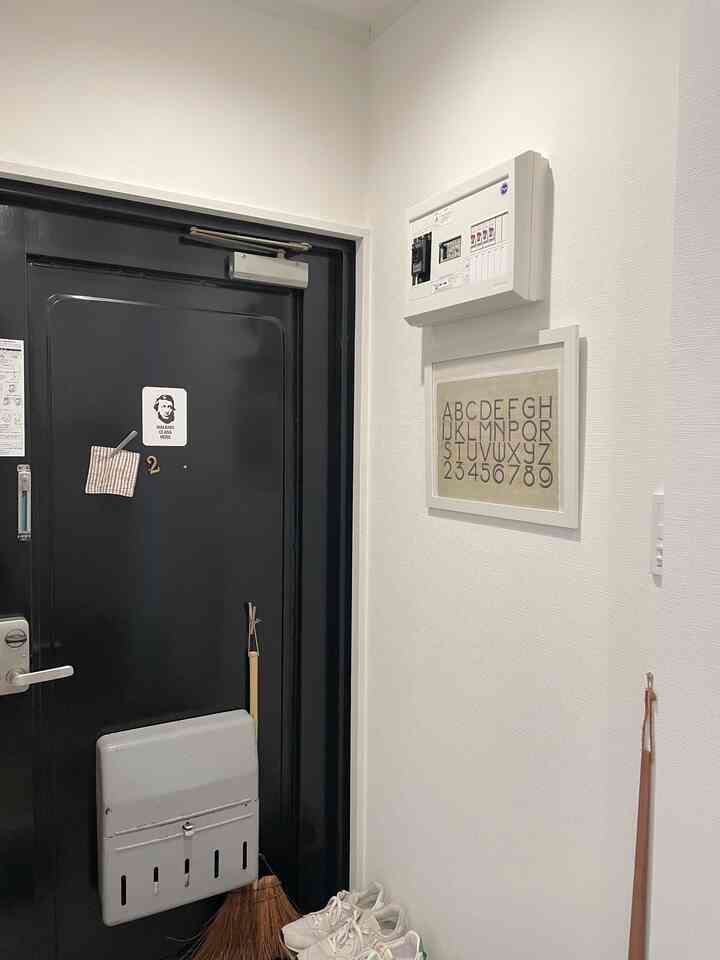 白い壁と黒い玄関ドア、靴とほうきが置かれたシンプルな玄関スペース