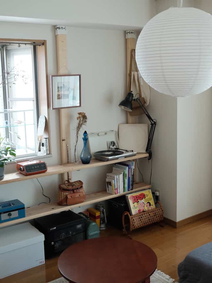 Small living room with white and natural wood tones featuring wooden shelves and a round table in a natural modern interior