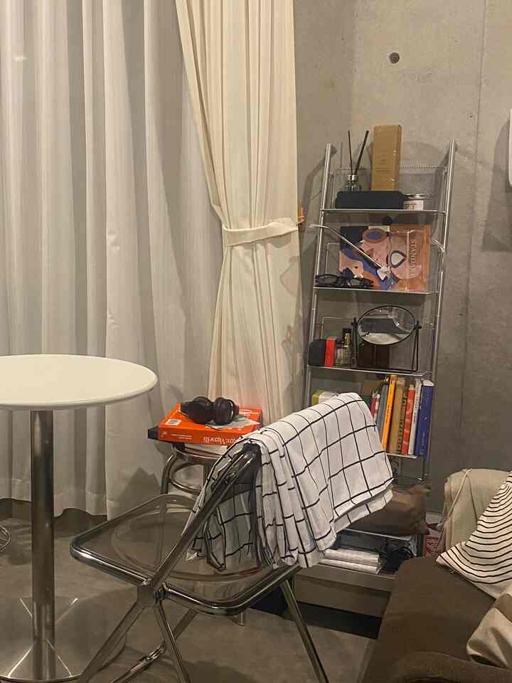 Narrow space with silver metallic furniture and white curtains, featuring a round table, chair, and ladder shelf with books and accessories in a natural home office setting
