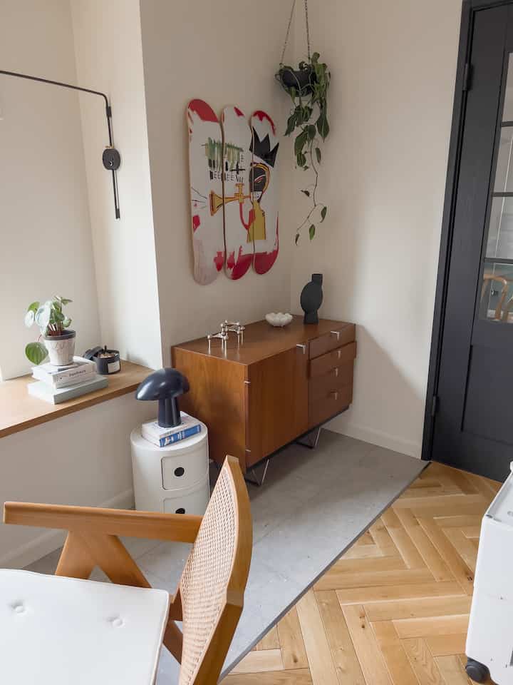 Natural wood tones and beige living room featuring a wooden cabinet, nightstand, wall art, and plants in a cozy atmosphere